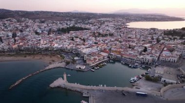Yunanistan 'ın Girit kentinin pitoresk mimarisinin üzerinde güneş batarken Chania limanının nefes kesici güzelliğini deneyimleyin. Canlı renkler, bu tarihi yerin çarpıcı bir manzarasını oluşturuyor..