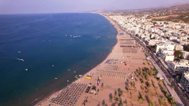 Girit 'in nefes kesici hava manzarasına tanık olun. Kumlu kumsallar, berrak mavi sular ve kıyı boyunca güneş panjurları ve şemsiyelerle kaplı canlı deniz manzarası..