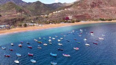 Tenerife 'nin nefes kesici hava manzarasına tanık olun, berrak mavi sulara saçılmış canlı tekneleri sergiliyor. Arkaplanda dağlar olan güzel sahil şeridinin tadını çıkar..