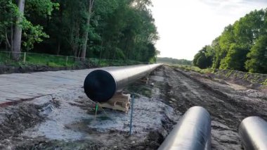 İnşaat ekipleri ağaçlık bir bölgeye bir doğalgaz boru hattı kurarak, temiz bir patika boyunca büyük siyah borular döşemek için ekipman kullanıyorlar. Projede enerji dağılımının artırılması hedefleniyor.