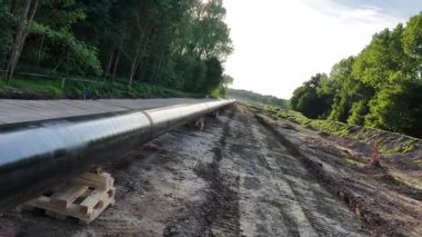 İnşaat ekipleri ormanlık bir bölgeye aktif olarak yeni bir doğalgaz boru hattı döşüyorlar. Ağır makineler görünür ve açık hava koşulları bölgenin görüş mesafesini artırıyor..