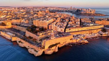 Valletta, Malta 'nın zengin tarihini, etkileyici binalarını ve gün batımının sıcacık parıltısıyla vurgulanan güzel sahil şeridini gösteren havadan bir perspektifini deneyimleyin..