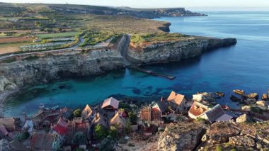 Malta 'da büyüleyici bir balıkçı köyünün nefes kesici hava perspektifini keşfedin. Gün boyunca evlerin canlı renklerini, engebeli uçurumları ve berrak mavi gökyüzünün altındaki sakin suları keşfedin..