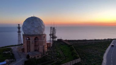 Malta üzerinde çarpıcı bir kıyı manzarası olan bir hava manzarası deneyin. Tarihi radar istasyonu gün batımına karşı duruyor, aşağıdaki dingin suları aydınlatıyor..