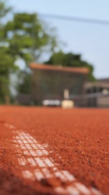 Kırmızı kil kort mesafeye uzanıyor, desenli yüzeyi gözler önüne seriyor. Oyuncular pratik yaparken ağaçlar gölge sağlar. Açık gökyüzü bu açık hava sporunun atmosferini arttırıyor..