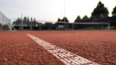 Kırmızı kil tenis kortu taban çizgisine yakın çekim ile vurgulandı. Güneş ağaçların arkasında batar, sıcak ışık yayar, oyuncular için sakin bir atmosfer yaratır..