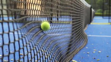 Oyuncular öğleden sonra mavi bir tenis kortunda pratik yaparlar. Oyuncular yeteneklerini geliştirdikçe oturumun şiddetini vurgulayan bir tenis topu ağın yanında duruyor..