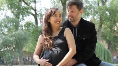 Neşeli bir çift, aileye katılacakları günü kutlarken parkta birlikte vakit geçirmekten zevk alıyor. Sıcak güneş onların mutlu anlarını ve gülümsemelerini arttırır..