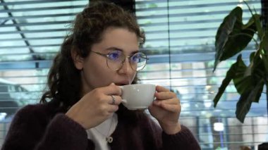 Bir insan bir kafede rahatça oturup bir fincan kahvenin tadını çıkarıyor. Güneş ışığı panjurların arasından akar, rahatlatıcı bir atmosfer yaratır. Rahatlamak ve anın tadını çıkarmak için mükemmeldir..