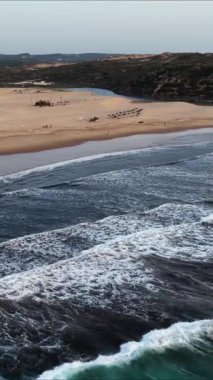 Güney Portekiz 'de dalgaların nazikçe çarptığı ve insanların manzaralı kıyı şeridinden keyif alırken görülebildiği çarpıcı bir kumsal manzarasını keşfedin. Doğada sükuneti tecrübe et..