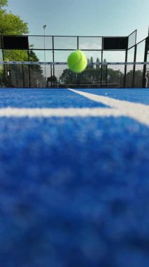 Canlı bir mavi tenis kortu havada uçan bir tenis topunun hareket anını yakalar..