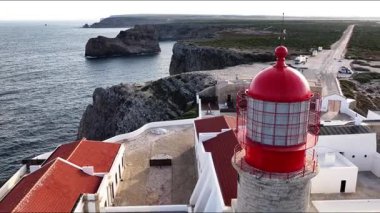 Portekiz 'in güneybatı ucu Cape St. Vincent' ın nefes kesici manzarasına tanık olun. İkonik kırmızı deniz feneri dramatik uçurumlara ve güneş batarken engin Atlantik Okyanusuna bakıyor..
