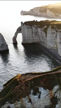Güneş batarken Etretat, Normandiya 'nın nefes kesici uçurumlarını keşfedin, denizin üzerinde büyülü bir parıltı yaratın ve manzaranın engebeli güzelliğini artırın..