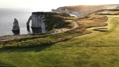 Etretat, Fransa 'nın dramatik uçurumların denizle buluştuğu nefes kesici güzelliğini tecrübe edin. Akşam ışığı yemyeşil golf sahasını güçlendiriyor ve unutulmaz bir manzara yaratıyor..
