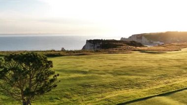 Fransa 'nın Etretat kentinin güzelliğini hissedin. Altın güneş ışığı yemyeşil golf sahalarının üzerine sıcacık bir ışık saçıyor..