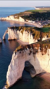 Çarpıcı hava perspektifi, Normandiya kıyıları boyunca Etretat 'ın ikonik uçurumlarını yakalar. Altın gün batımı, tebeşir kayalıklarının ve aşağıdaki sakin suların üzerine ılık renkler döküyor..