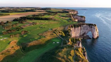 Etretat 'ın beyaz tebeşir kayalıkları, canlı yeşil alanlar ve Fransa' daki bu büyüleyici yerin üzerinde güneş batarken sakin kıyı şeridinin nefes kesici hava perspektifini tecrübe edin..