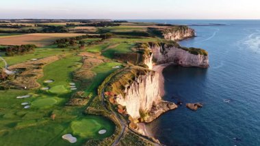 Etretat ikonik uçurumlarının ve yukarıdan gelen bereketli manzaranın nefes kesen manzarası. Gün batımının altın renkleri sahili aydınlatıyor ve doğal güzellikleri gözler önüne seriyor..