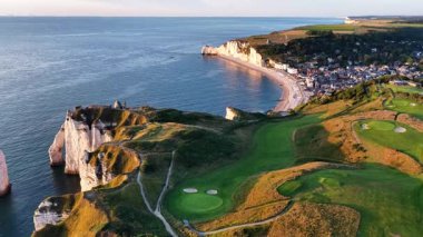 Fransa 'da Etretat' ın çarpıcı hava perspektifini keşfedin, görkemli uçurumlar, sakin bir plaj ve sahil boyunca uzanan geniş bir golf sahası, gün batımının ılık ışığında yıkanan.