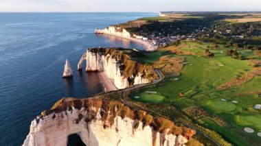 Etretat, Fransa 'nın büyüleyici hava manzarasını deneyin. Ünlü beyaz uçurumlarını, yemyeşil golf sahalarını ve büyüleyici sahil şeridi boyunca gün batımında canlı kıyı kasabasını vurguluyor..