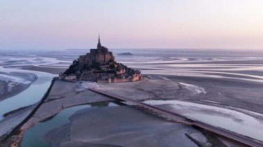 Fransa 'nın Normandie şehrinde şafak sökerken Abbaye du Mont-Saint-Michel' in hava manzarasını deneyin. İkonik yapı dramatik bir şekilde suyun ve kumlu sahillerin üzerinde yükselir ve tarihi cazibesini ortaya çıkarır..