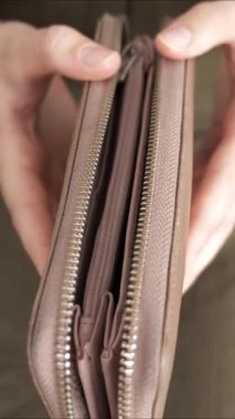 Eller fermuarlı bir cüzdan tutarken gösteriliyor. İç bölmeleri ve eşsiz tasarım unsurlarını göstermek için fermuarını dikkatlice açıyorlar. Malzeme ışığı hafifçe yansıtıyor..