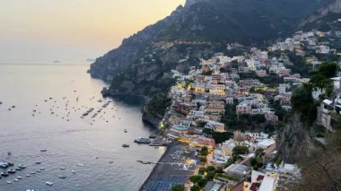 Güneş batarken Amalfi Sahili boyunca Positano 'nun güzelliğini hissedin, gökyüzünü değiştirin ve kayalıklara kurulmuş resimli köyü aydınlatın. Tekneler suda huzur içinde sürükleniyor..