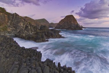 Okyanus Dalgaları, Mor Gökyüzü ve Engebeli Arazide Serenely Akan Bulutlar ile Alacakaranlık 'ta Rocky Coast' a çarpıyor. Telawas Plajı Lombok Endonezya