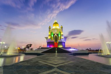 view of the mosque monument shining with bright colors underneath there is a fountain that comes out of the pool at dusk and the purplish blue sky with thin clouds at the Gerung Monument clipart