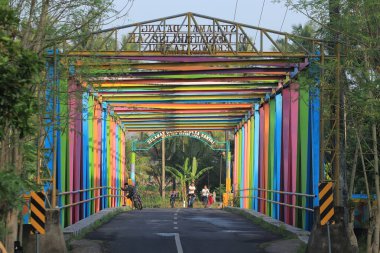 Colorful Bridge Spans River Connects Communities Vibrantly in Rural Landscape clipart