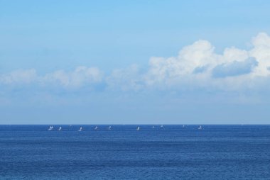 Yelkenliler, güneşli bir günde Bulutlu bir gökyüzünün altında Mavi Okyanusta süzülür.