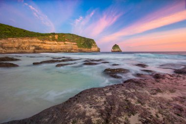 Coastal Cliffs Meet Ocean Waves at Sunset with Colorful Sky and Rocky Beach Tranquility in Bilasayak Beach, Lombok, Indonesia. clipart