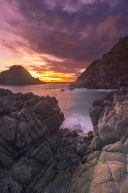 Güneş ışığına maruz kaldığı için kırmızımsı olan mavi deniz manzarası Telawas sahilinde, Lombok, Endonezya 'da alacakaranlıkta sıralanmış siyah kayalar.