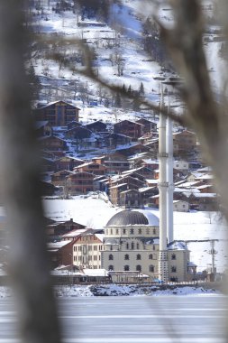 Winter Village Reflects in Icy Lake with Mosque and Snowy Landscape Beautifully Mirrored Upside Down in Winter Scene. clipart