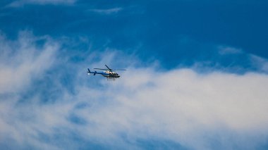 Mavi helikopter mavi gökyüzündeki beyaz bulutların arka planına karşı