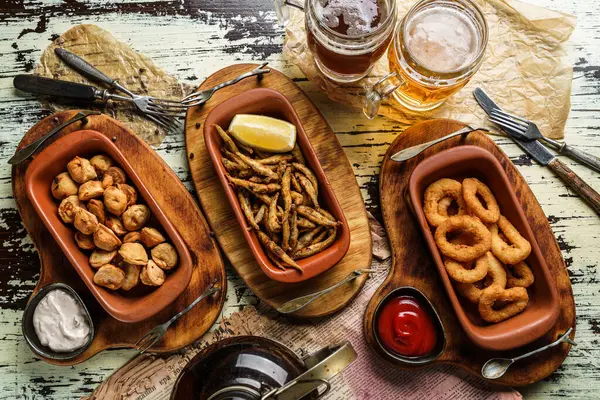 Crunchy fried squid rings breaded, fried anchovies in cornmeal, fried dumplings and glasses of beer in wooden background, beer snacks set for party, top view
