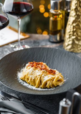 Masada parmesanlı peynirli makarna, bir bardak şarapla arka planda bokeh, ışık çelengi ve sim. Tatil yemeği, Noel yemeği, yakın çekim, seçici odaklanma.