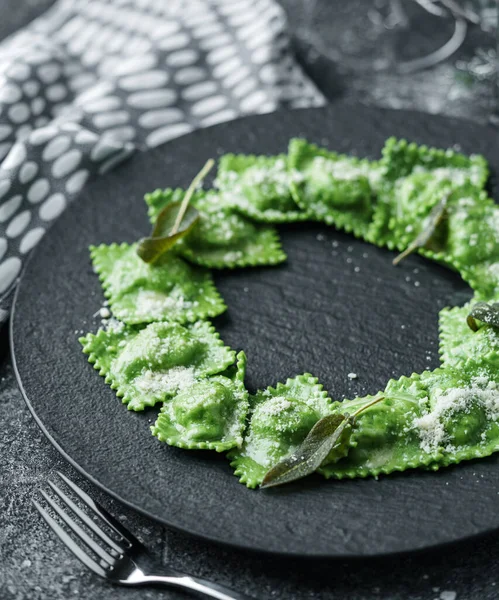 Green ravioli with spinach and ricotta cheese on plate over dark holiday background with glass of wine. Merry Christmas and New Year meal, vegetarian dishes, close up, bokeh
