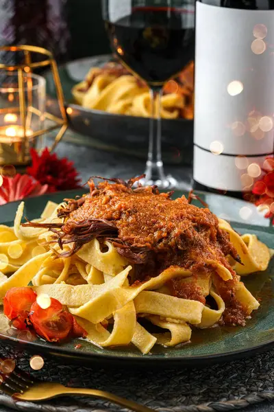 Holiday pasta bolognese with meat and sauce in the plate on the holiday table with glasses, bottle of wine, candles, festive decoration, garland, flowers. Christmas and New Year dinner bokeh, lights