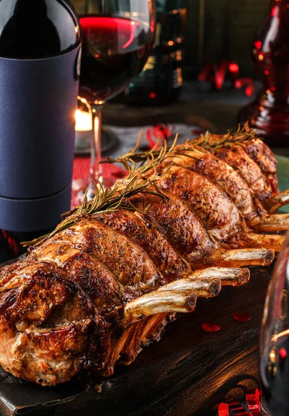 Holiday baked meat tenderloin with ribs, pork, roast beef on dark wooden board with glasses, bottle of wine, candles, festive decoration. Christmas and New Year food, bokeh, lights