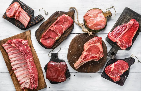 Set of various raw meat steaks. Fresh meat of beef, pork, veal, chicken, steak t-bone, rib eye, tomahawk, ribs, tenderloin on cutting board over white background. Meat food, butcher shop, top view