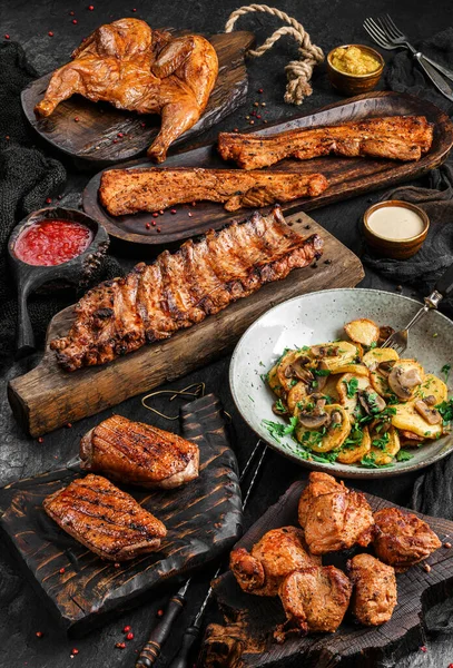Grilled chicken or quail, meat tenderloin, fried ribs, shish kebab, fillet and fried potatoes with mushrooms on wooden boards over dark stone background. Meat food, top view