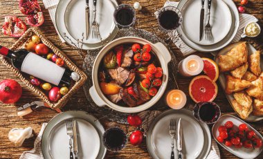 Paskalya bayramı masası, şarap bardakları, Paskalya pastası, renkli yumurtalar, sebzeli fırında et, ahşap arka planda akşam yemeği için lahana ruloları. Tatil konsepti, üst görünüm, ton