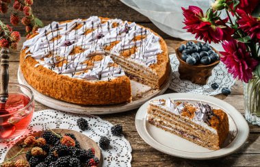 Kremalı lezzetli bisküvi keki ve ahşap kırsal arka planda bir fincan çay, çiçekler, dantel peçeteler. Tatlılar, tatlı ve pasta, ev yapımı kekler, yakın plan, seçici odaklanma