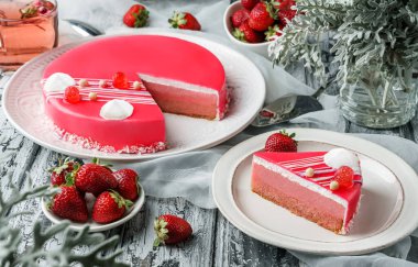 Ayna jöleli pembe kremalı pasta, arka planda hafif çay, çilek ve çiçeklerle birlikte krema ve böğürtlen. Tatlılar, tatlı ve pasta, üst manzara