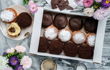 Vanilyalı, çikolatalı, pudra şekerli ve çikolatalı çörekler gri arka planda, çiçekli karton kutuda. Tatlılar, tatlı ve pasta, üst manzara