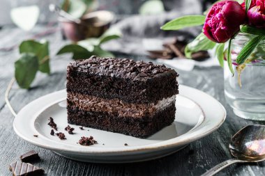 Koyu arka planda çikolata parçalı çikolatalı kek ve şakayık çiçekleri. Tatlılar, tatlı ve pasta, yakın çekim, seçici odaklanma