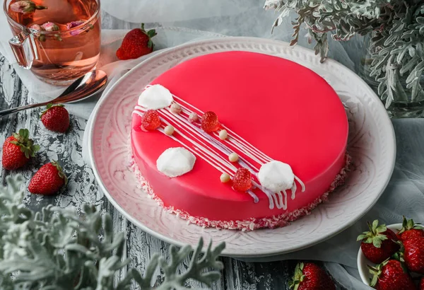 Pink mousse cake with mirror glaze, meringues and berries on light background with cup of tea, strawberries and flowers. Sweets, dessert and pastry, top view