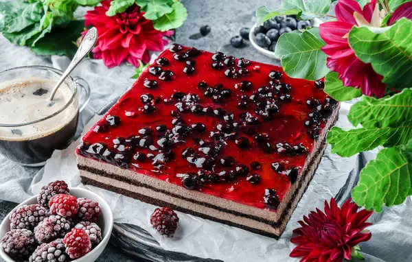 Chocolate mousse cake with berry jelly on grey background with cup of coffee, berries and red flowers. Sweets, dessert and pastry, top view