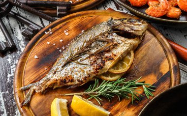 Baharatlı, limonlu ve biberiyeli ızgara dorado balığı ahşap kırsal arka planda tahtayı kesiyor. Deniz ürünleri, sağlıklı yiyecekler, yakın çekim.